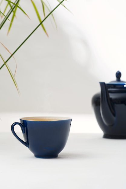 Chá em uma xícara de cerâmica azul escura e um bule em uma mesa branca Fundo claro