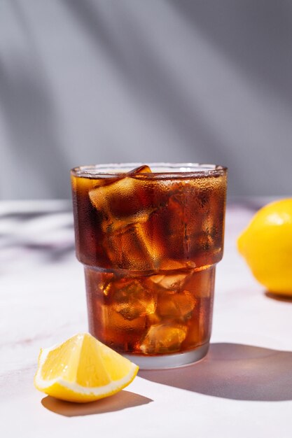 Chá gelado Cuba Libre ou Long Island coquetel com cola limão e gelo em um copo em fundo de mármore com sombra O conceito de uma bebida refrescante fria ou limonada