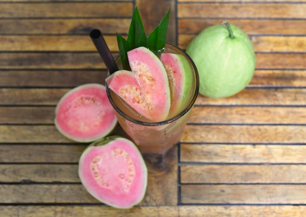 Chá gelado de goiaba rosa no fundo da mesa de madeira com goiaba fatiada