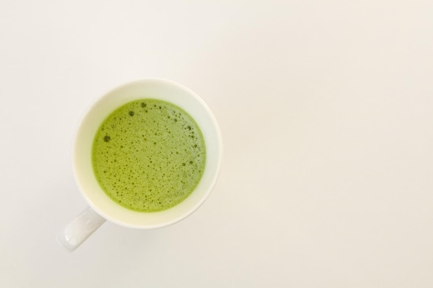 Chá Matcha em uma xícara branca sobre um fundo branco. Lugar para texto.