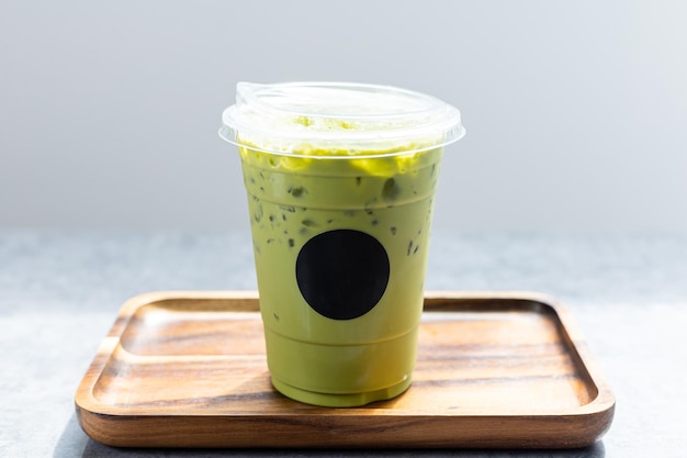 Chá matcha verde gelado na bandeja de madeira com adesivo preto do logotipo. chá verde com leite em copo de plástico.