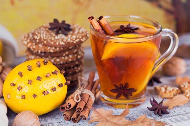 Chá quente de outono com limão e especiarias em copo de vidro. Chá saudável com biscoitos, nozes e folhas ao redor. Conceito de outono