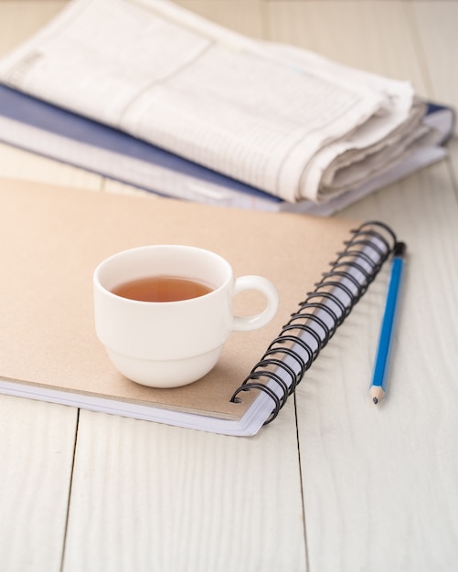 Chá quente em um caderno em uma mesa de madeira branca.