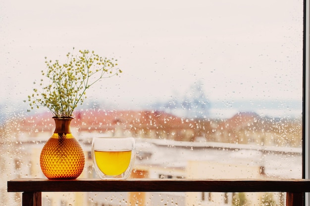 Chá quente em vidro térmico na janela de fundo com pingos de chuva