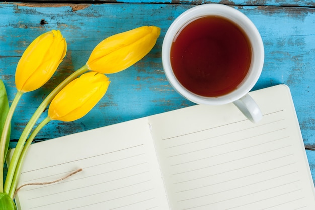 Chá, tulipas e caderno na mesa azul