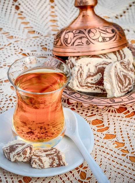 Chá turco em um copo de vidro e halva de mármore em uma mesa com uma toalha de mesa artesanal e fabricante de doces