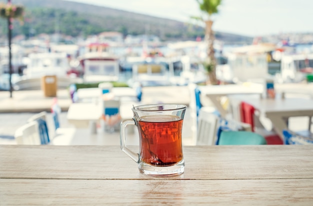 Chá turco no copo de vidro tradicional na mesa de madeira com a vista de fundo da marina do mar