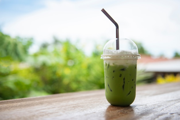 Chá verde gelado em copo de plástico / matcha frappe de latte de chá verde e palha na mesa de madeira com a natureza