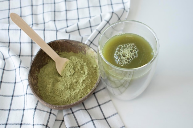 Chá verde matcha em pó e fabricado em um fundo branco com uma toalha de cozinha quadriculada branca