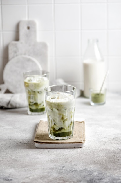 Chá verde matcha gelado com leite e gelo em uma mesa cinza