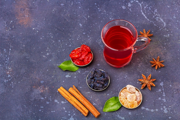 Chá vermelho (rooibos, hibisco, karkade) na xícara de chá turco (armudu) com dogwood, passas, açúcar em estilo oriental em fundo escuro. Chá de ervas, vitaminas e desintoxicação para resfriado e gripe