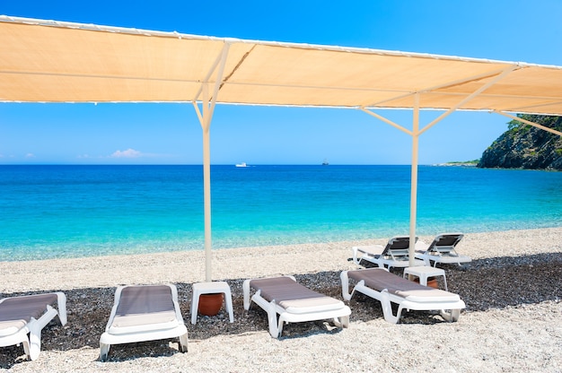 Chaiselongues unter dem Zelt am Kiesstrand in Kemer, Türkei.