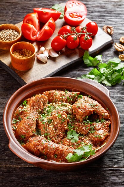 Chakhokhbili guisado de tomate de frango com ervas frescas nozes e especiarias em uma panela de barro em uma mesa de madeira cozinha georgiana vista vertical