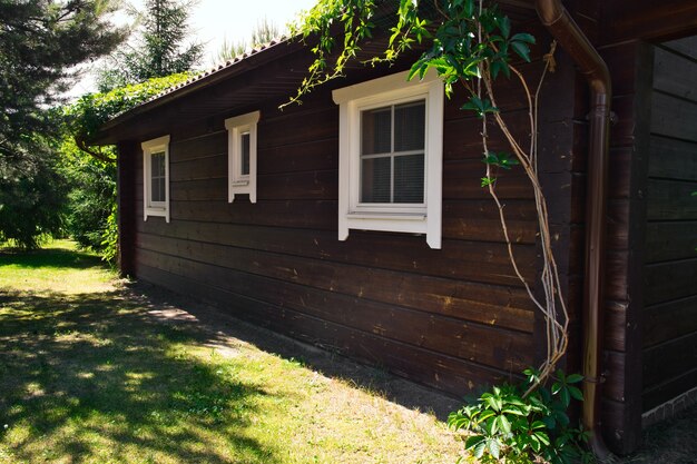 Chalé de madeira escura simples em dia ensolarado de verão. a parede da casa de hóspedes com três janelas. férias, fim de semana, recreação na natureza.