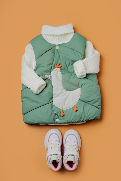 Chaleco verde con suéter cálido sobre fondo naranja. Prendas de abrigo para niños con estilo. Traje de moda de invierno