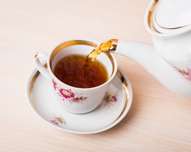 Chaleira de porcelana estilo antigo derramando chá do jarro para a xícara de chá