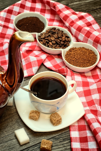 Chaleira velha para café, xícaras de café em um fundo de madeira com um pano vermelho branco