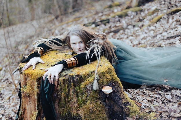 Chamã feminina na natureza da floresta prístina deitada no tronco da árvore jóias de ouro cabelo peludo