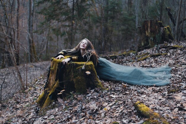 Chamã feminina na natureza da floresta prístina sobre um tronco de árvore verde jóias de ouro cabelo peludo