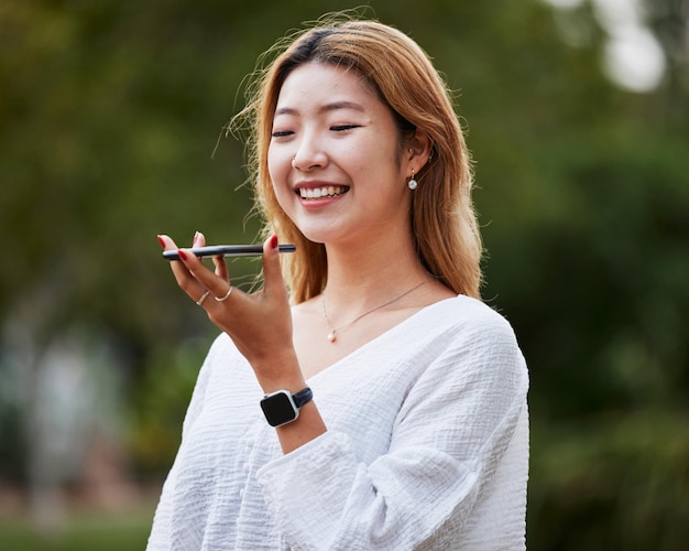 Chamada de áudio feliz e uma mulher na natureza para bate-papo de comunicação ou instrução de voz Smile park e uma garota asiática falando em um celular para gravação de áudio em rede ou conversa