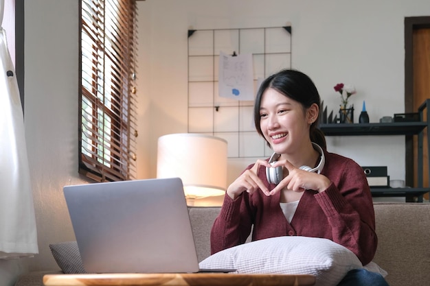 Chamada de vídeo atraente jovem sorridente por laptop no sofá em casa conceito de estilo de vida