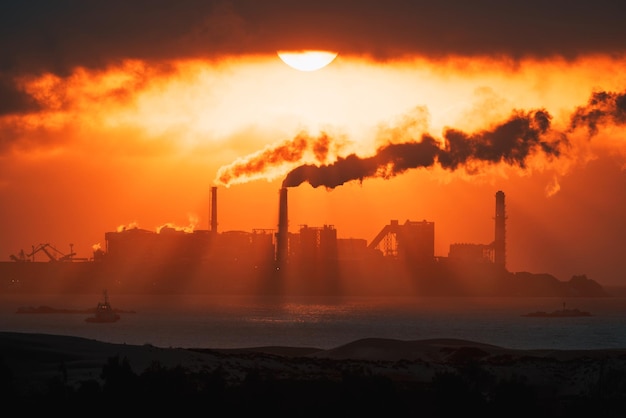 Chaminés termoelétricas expelem vapor ou fumaça em um pôr do sol ardente na costa do oceano