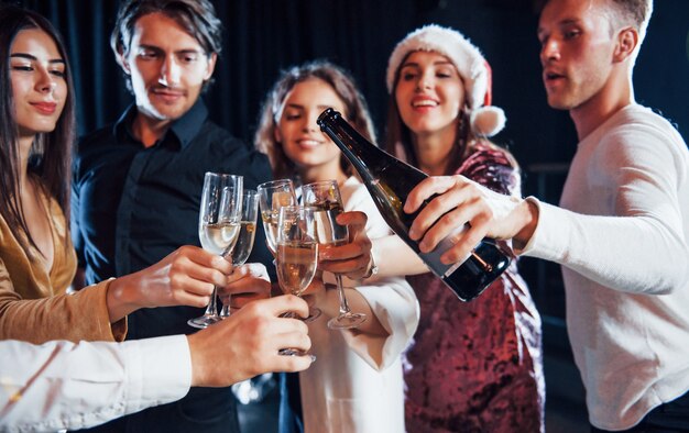 Champagner gießen. Gruppe fröhlicher Freunde, die das neue Jahr drinnen mit Getränken in den Händen feiern.