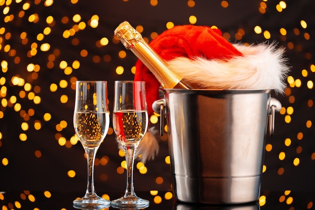 Champagner und Weihnachtsmannhut auf unscharfer Girlandenhintergrund-Vorderansicht