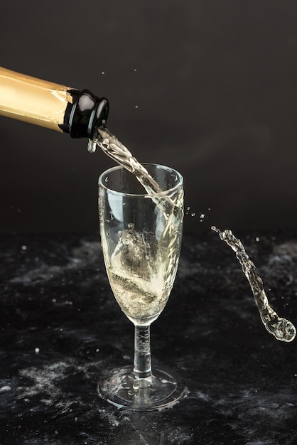 Champagner wird gegen schwarzen Hintergrund in ein Glas gegossen