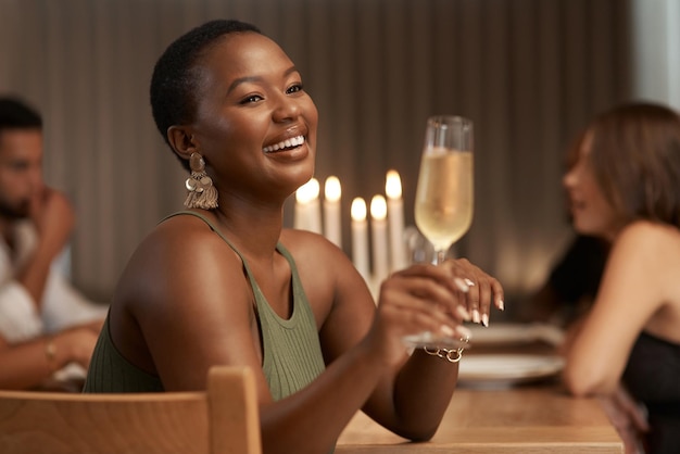 Champagnerfeier und glückliche schwarze Frau auf einer Party oder Abendessen an einem Tisch im Speisesaal Glückslächeln und afrikanische Dame, die ein Glas alkoholisches Getränk bei einer Neujahrsveranstaltung in einem Haus genießt