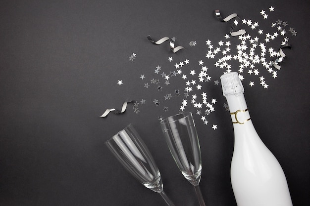 Foto champagnerflasche, gläser und konfetti auf dunklem hintergrund. flache lage der feierkomposition.