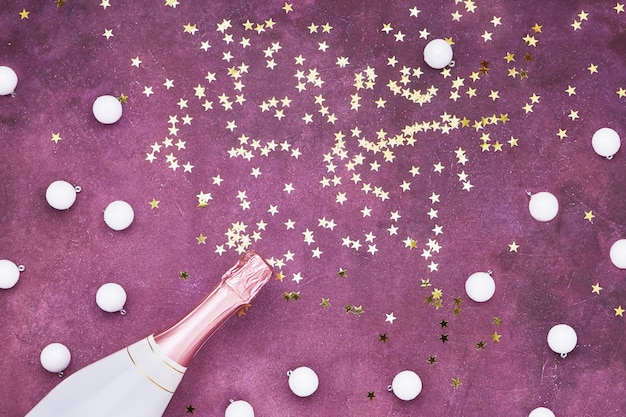 Champagnerflasche mit goldenem Konfetti auf lila Wand. Flache Lage der Weihnachtsfeier