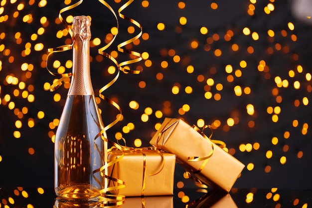 Champagnerflasche und verpacktes Geschenk auf unscharfem Hintergrund der Vorderansicht der Weihnachtsbeleuchtung