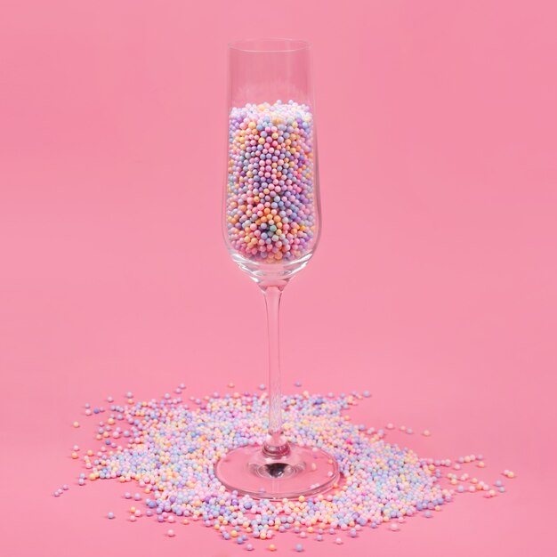 Champagnerglas gefüllt mit bunten Zuckerkugeln auf rosa