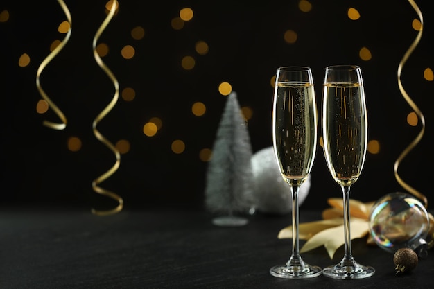 Champanhe delicioso em copos e decoração de Natal em mesa preta contra luzes borradas espaço para texto