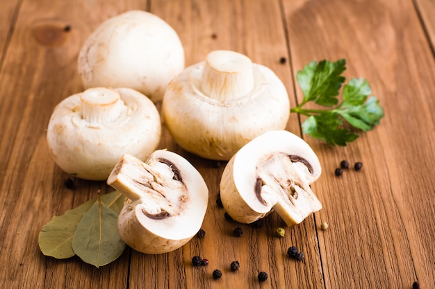 Champignon fatiado e inteiro, folha de louro, salsa e pimenta preta em uma mesa de madeira