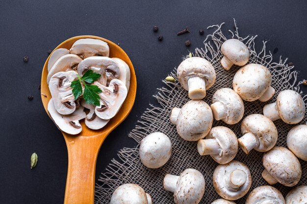 Foto champignon fatiado fresco com salsa na colher de pau e cogumelos maduros brancos em um surfce preto para cozinhar pratos deliciosos caseiros.