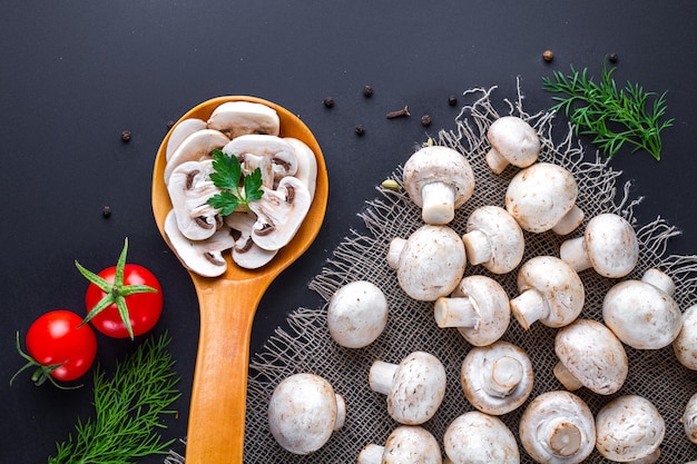 Champignon fatiado fresco na colher de pau e grupo de cogumelos maduros brancos em um surfce preto para cozinhar pratos caseiros.