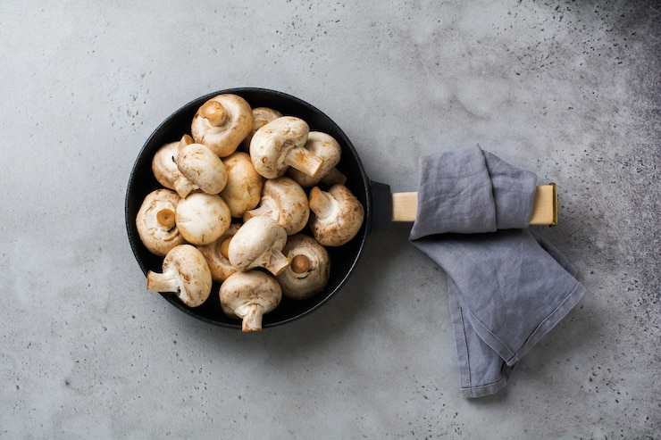 Foto champignon mit rohen pilzen in einer alten gusseisernen pfanne auf einem alten rustikalen tisch aus grauem beton zum braten. draufsicht.