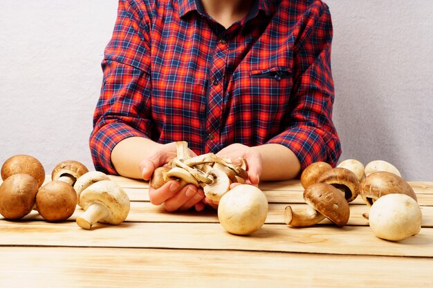 Champignon na mão. Uma garota com uma camisa quadriculada vermelha tem cogumelos frescos nas mãos sobre um fundo de madeira.