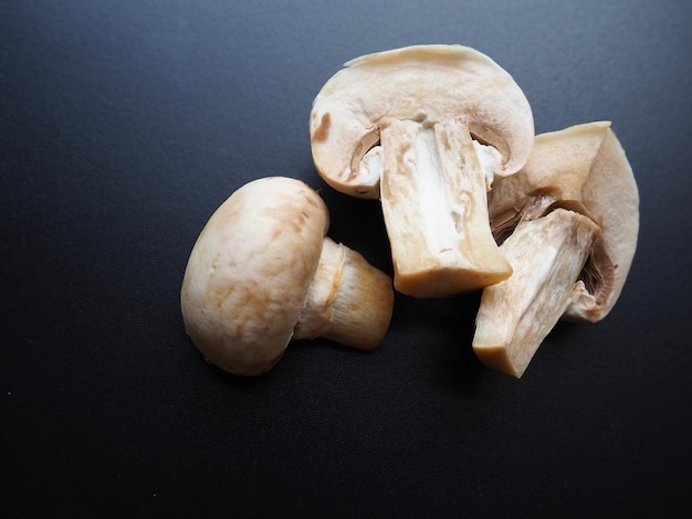 Champignons auf schwarzem Hintergrund Geschnittene und ganze frische ungekochte rohe Pilze Kochen von Pilzen mit einem Rezept