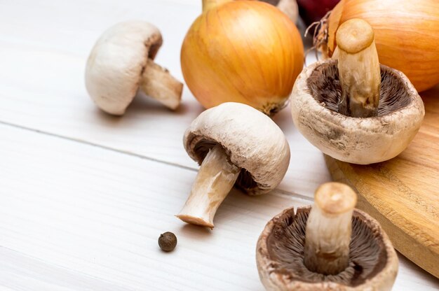 Champiñones y cebollas con tabla de cortar en la mesa de madera blanca