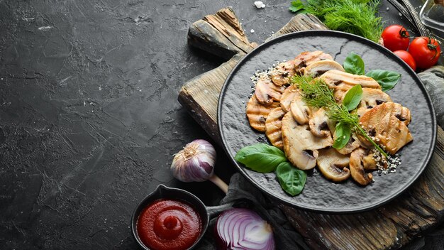 Champiñones fritos con sésamo y albahaca en un plato negro sobre fondo negro Vista superior Espacio libre para el texto