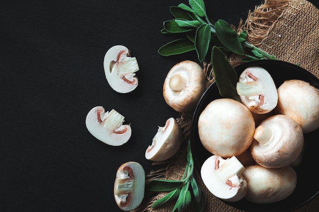 Champiñones y hierbas enteros y cortados sobre un fondo negro. Primer plano, endecha plana, vista superior. Fondo de alimentos, enfoque selectivo.