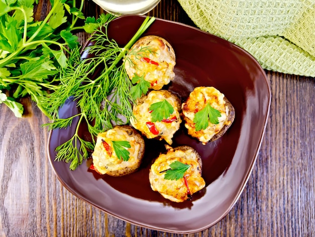 Champiñones rellenos de carne con perejil y pimienta en un plato marrón, toalla de cocina verde en el fondo de las tablas de madera en la parte superior