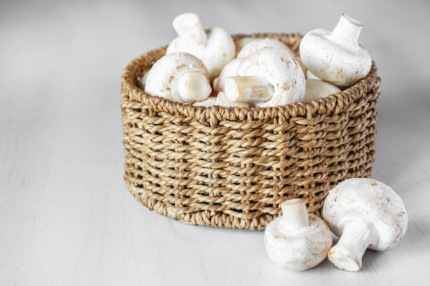 Champiñones de setas en una cesta de mimbre redonda sobre una mesa de madera blanca