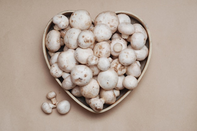 Champiñones sucios naturales blancos frescos aislados en caja de corazón de madera. Comida ecológica saludable.