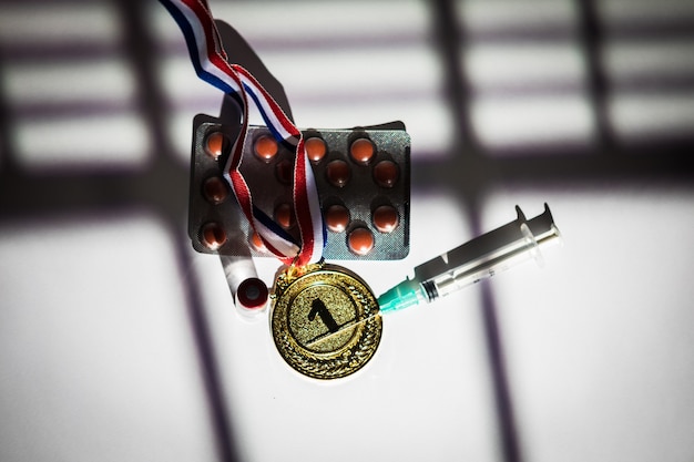 Champion Goldmedaille, Dopingmittelspritze, Tablettentablette und Fläschchen mit verbotenen Substanzen mit Licht und Schatten eines Vorhangs, der durch das Fenster eindringt. Sport- und Dopingkonzept