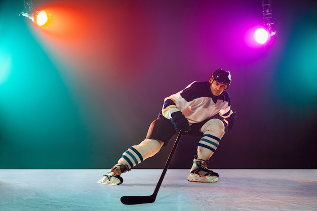 Champion. Männlicher Hockeyspieler auf Eisplatz und dunklem neonfarbenem Hintergrund mit Taschenlampen. Sportler in der Ausrüstung, Helmübungen. Konzept des Sports, des gesunden Lebensstils, der Bewegung, des Wellness, der Aktion.