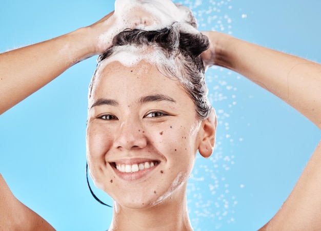 Champú y ducha de mujer en retrato de estudio con limpieza de cuidado del cabello y sonrisa de fondo azul Modelo de cabello y bienestar con jabón de espuma o agua para cosméticos de autocuidado o belleza con felicidad